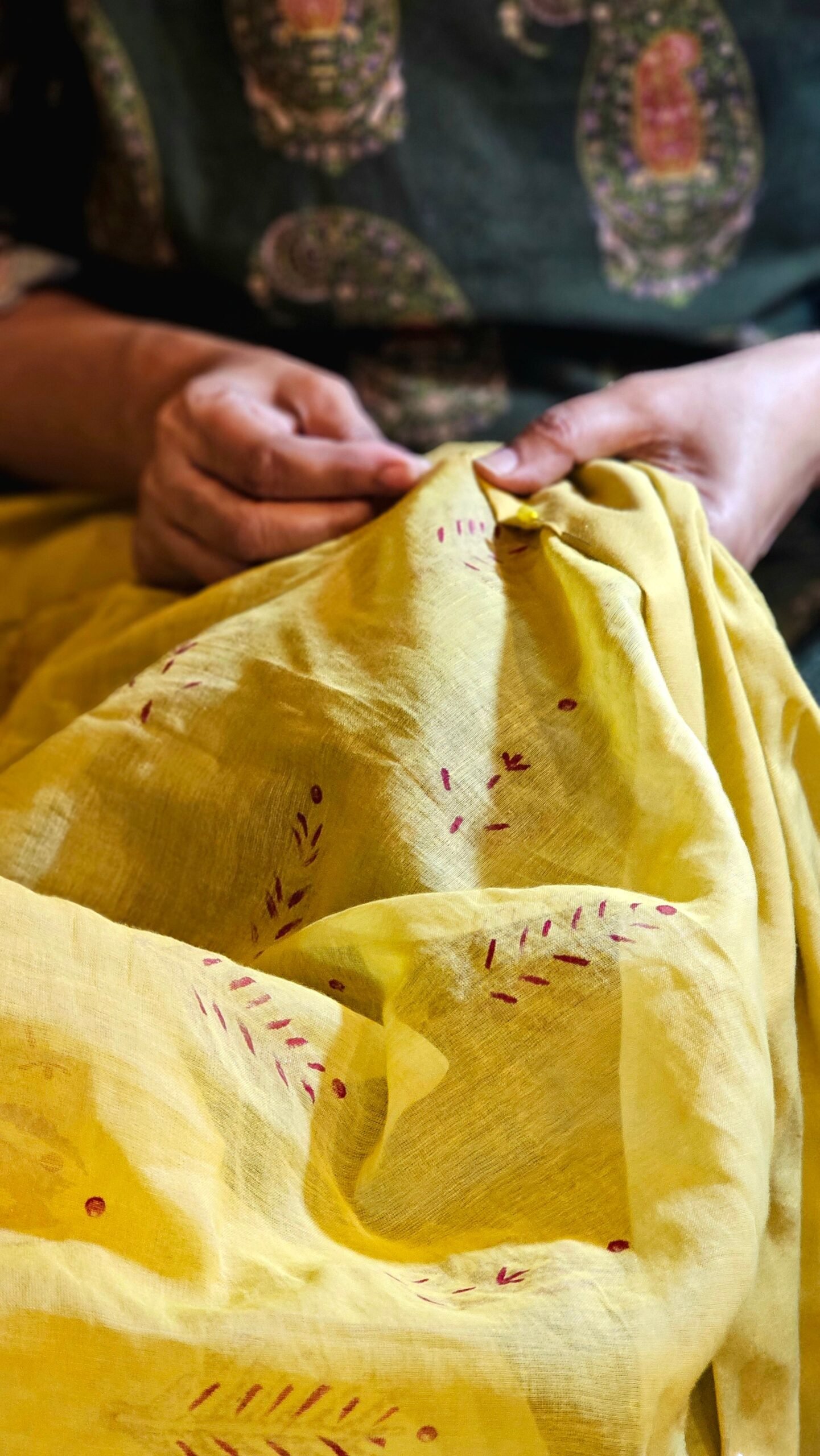 Close-up of artisan hands sewing yellow fabric with embroidered patterns, showcasing craftsmanship.