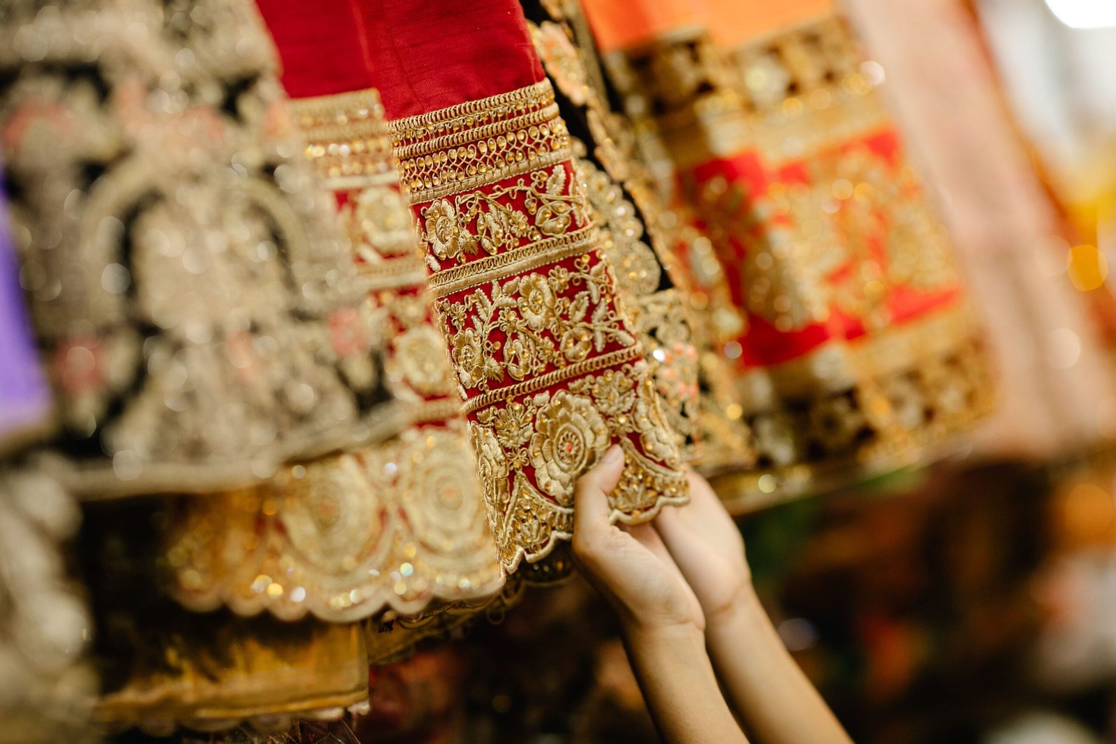 A detailed close-up of hands feeling intricately embroidered fabric in a vibrant market setting.